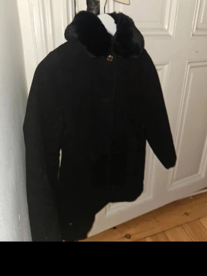 Svart pälsjacka med krage - Säljer en svart pälsjacka med mjuk, fluffig krage och rak passform. Jackan har en enkel knäppning framtill och är tillverkad i ett pälsliknande material som ger en lyxig känsla. Perfekt för dig som vill ha en stilren och varm jacka till vintern.