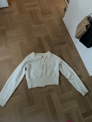 Vit kofta med knappar - En stilren vit kofta med knappar framtill. Koftan har en ribbad nederkant och är gjord i ett mjukt stickat material som känns skönt mot huden. Perfekt för att slänga över en topp när det är lite kyligt.