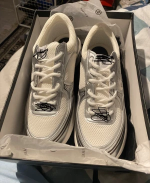 Vita sneakers med silvriga detaljer - Snygga vita sneakers med silvriga detaljer och tjock sula. Ovandelen är i mesh och syntetmaterial för en sportig look. Skorna har vita snören och svartvit yttersula med bra grepp. HÖR AV DIG OM DU VILL HA MER BILDER ELLER DISKUTERA PRISET😊 skickar k om 24 Tim