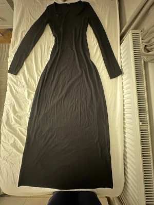 Svart långklänning från BikBok - En svart långklänning från BikBok med långärmad design och figurnära passform. Klänningen är enkel och stilren, perfekt för dig som gillar minimalistiska plagg. Materialet är mjukt och stretchigt, vilket gör den bekväm att bära hela dagen. Aldrig använt