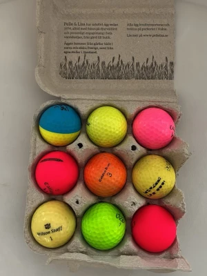 Färgglada golfbollar  - Säljer ett set med nio golfbollar i olika färger som neonrosa, gul, orange, grön och blå/gul. Bollarna levereras i en äggkartong och har olika märken och tryck. Perfekt för dig som vill ha extra synliga golfbollar på banan.