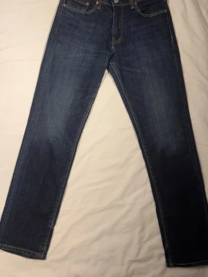 Mörkblå raka jeans från Levi's - Säljer ett par klassiska mörkblå jeans från Levi's med raka ben och femficksdesign. Jeansen har kontrastsömmar och är tillverkade i slitstark denim. Perfekt för dig som gillar en tidlös och enkel look.