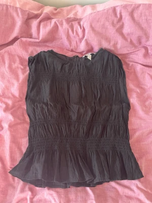 Svart blus  - Svart blus från H&M med smockade detaljer och volang nertill. Storlek S