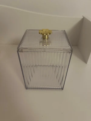 Transparent burk med guldfärgad knopp från SHEIN  - Fyrkantig transparent burk i plast med räfflade sidor från SHEIN. Locket har en guldfärgad blomformad knopp. Perfekt för förvaring av småsaker eller smycken.
