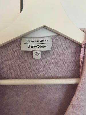 Ljuslila kofta från & Other Stories - Mysig ljuslila kofta från & Other Stories Los Angeles Atelier. Koftan har en mjuk, stickad känsla och omlottmodell med långa ärmar. Perfekt för lager på lager och en chill look.