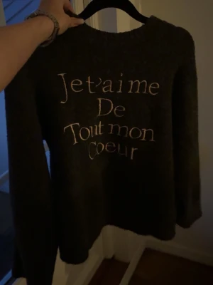 Mörkgrå stickad tröja med text - Kan gå ner vid snabb affär.Mysig mörkgrå stickad tröja med vit broderad text 'Je t'aime de tout mon coeur' på framsidan använd cirka 2-3 gånger 
