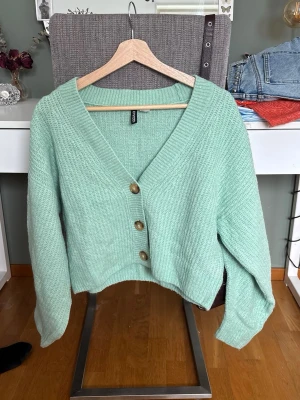 Mintgrön kofta från H&M Divided - Säljer en mintgrön kofta från H&M Divided i storlek L. Men passar mig som vanligtvis har S. Koftan är stickad med v-ringning och har tre stora bruna knappar framtill. Den har långärmad design och en loose passform 