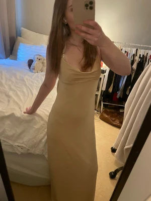 Champagnefärgad långklänning med öppen rygg - Säljer en elegant champagnefärgad långklänning med smala axelband och snygg drapering vid bysten. Klänningen har en öppen rygg och är figurnära med slätt material som ger en lyxig känsla. Perfekt för dig som vill ha en stilren och modern look.