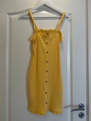 Gul ribbad kortklänning med knappar - Säljer en  gul ribbad klänning med knappar. Perfekt till sommaren. Säljer för att den inte kommer till användning längre. 