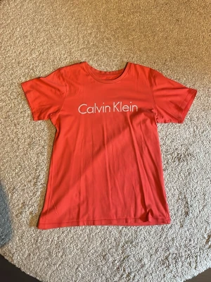 Röd Calvin Klein t-shirt i bomull - Snygg röd t-shirt från Calvin Klein med klassisk logga tryckt framtill. Tillverkad i mjuk bomull och har en normal passform med korta ärmar och rund hals. Perfekt för en clean och stilren look.