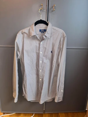 Grå skjorta från Polo Ralph Lauren - Klassisk grå skjorta från Polo Ralph Lauren med lång ärm och knappar framtill. Skjortan har en liten broderad logga på bröstet och är tillverkad i bomull. Perfekt för en clean och stilren look. Button down