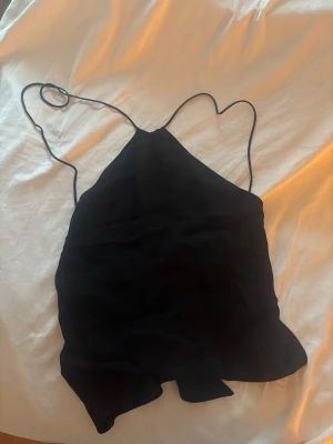 Svart halterneck topp från zara - Snygg svart linnetopp från Zara med tunna axelband och halterneck-modell. Toppen har en enkel och stilren design som passar perfekt till många olika looks. Materialet känns mjukt och lätt mot huden.