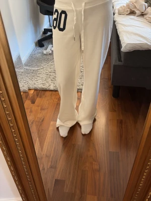 Vita mjukisbyxor från edikted - Säljer ett par vita mjukisbyxor från edikted med svart tryck '06' på ena höften. Byxorna har raka ben, dragsko i midjan och är tillverkade i mjukt material som känns skönt mot huden. Nypris runt 900 kr.