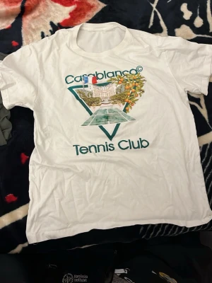 Casablanca - Säljer en vit t-shirt från Casablanca med stort tryck på bröstet som föreställer en tennisbana och texten 'Casablanca Tennis Club'. T-shirten har rund hals och korta ärmar. Perfekt för dig som gillar sportig och trendig stil.