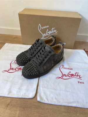 Grå mocka sneakers från Louboutin - HELT NYA!! Snygga grå sneakers från Christian Louboutin i mocka med coola nitar på tån. Skorna har snörning och en platt sula. Perfekta för dig som vill sticka ut med exklusiv design och detaljer. Först till kvarn!!!