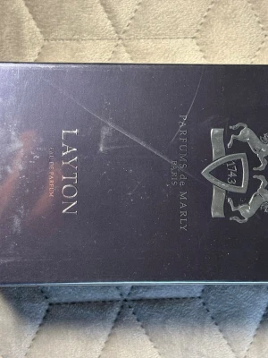 Parfums de Marly Layton EdP - Lyxig parfym från Parfums de Marly, modellen Layton. Flaskan har en elegant mörkblå färg med silverdetaljer och ett stilrent emblem på framsidan. Eau de Parfum med exklusiv och modern design, perfekt för dig som gillar unika dofter.