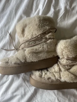 Beige fluffiga moon boots - Säljer ett par beige moon boots med supermjuk fuskpäls och höga sulor. Skorna har snörning runt skaftet och en chunky look som verkligen sticker ut. De är bara testade💗💗