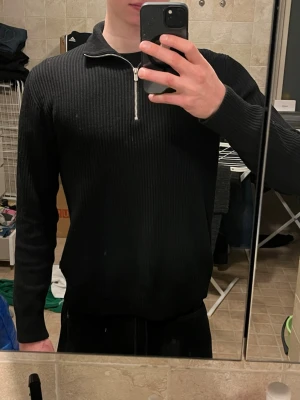 Svart ribbad halvzip tröja - Säljer en svart ribbstickad tröja med halvzip och hög krage. Tröjan har långa ärmar och är tillverkad i ett mjukt, stretchigt material. Stilren och perfekt när du vill känna dig lite extra snygg.