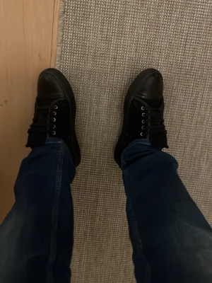 Svarta sneakers från Lanvin i mocka - Säljer ett par svarta Lanvin sneakers med ovandel i mocka och tå i skinn. Skorna har svarta snören, metallöglor och en platt sula. Klassisk och stilren design som passar till jeans eller andra byxor.