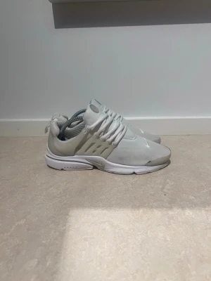 Nike vita Presto sneakers - Säljer ett par vita Nike Presto sneakers med mesh- och syntetmaterial. Skorna har en clean design med vita snören, diskret swoosh på tån och ventilerande detaljer på sidorna. Perfekta för dig som gillar minimalistisk stil och bekväma skor.