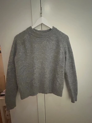 Grå stickad tröja från Zara - Mysig grå stickad tröja från Zara med rund halsringning och långa ärmar. Tröjan har en enkel, klassisk design och är perfekt för lager-på-lager under kyliga dagar. St S, 