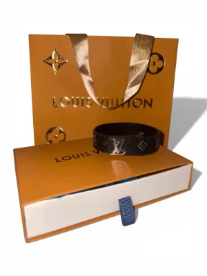 Louis Vuitton monogram armband - Snyggt armband från Louis Vuitton i läder med klassiskt monogrammönster och silverfärgade LV-detaljer. Armbandet har en stilren och exklusiv design som passar perfekt till din outfit. Levereras med originalförpackning och påse.