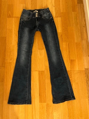 Blå bootcut jeans  - Snygga blå jeans från Girl Vivi med bootcut-modell och dekorativa metallknappar framtill. Jeansen har klassisk femficksdesign och slitna detaljer vid bensluten för en trendig look. 