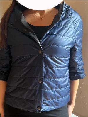 Mörkblå lätt dunjacka - Snygg mörkblå dunjacka med knappar framtill och diskreta horisontella sömmar. Jackan har en kortare, trekvarts figurnära modell och är i super skick!