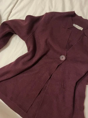 Vinröd kofta från SusyMix - Mysig vinröd kofta från SusyMix med en enkel knappstängning framtill och klassisk krage. Koftan har lång ärm och är tillverkad i ett mjukt, stickat material som passar perfekt för lager på lager. Enkel och stilren design som är lätt att matcha.