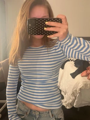 Randig långärmad topp i blått och vitt - Superfin långärmad topp med blå och vita ränder. Modellen är figurnära och har rund halsringning. Materialet är ribbat och stretchigt, vilket gör den både bekväm och snygg. Perfekt att styla med jeans eller kjol.