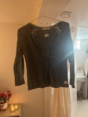 Mörkgrå stickad kofta från odd molly  - Snygg mörkgrå stickad kofta från odd molly med knytband framtill och fint hålmönster. Koftan har trekvarts ärmar, ribbade muddar och en avslappnad passform. Perfekt att slänga över en topp för en chill look.