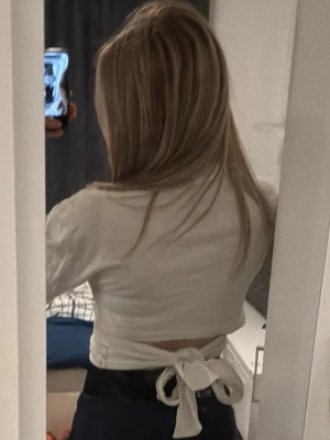 Vit omlottopp med knytband - Säljer en vit omlottopp med korta ärmar och breda knytband i ryggen. Toppen har en croppad passform och är tillverkad i mjukt bomullstyg. Lite öppen i ryggen och jätte najs när det är lite sol ute för tröjan är väldigt luftig 