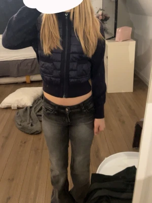 Mörkblå croppad pufferjacka - Snygg mörkblå croppad pufferjacka med dragkedja framtill. Jackan har quiltade partier på framsidan och långa ärmar i stickat material. Perfekt för dig som vill ha en trendig och sportig look.