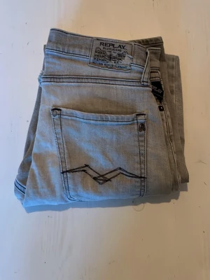 Ljusblå Replay jeans med brodyr - Säljer ett par ljusblå jeans från Replay med snygg svart brodyr på bakfickan och klassisk Replay-lapp i midjan. Jeansen har raka ben och är tillverkade i mjuk denim. Perfekta för en avslappnad och trendig look.