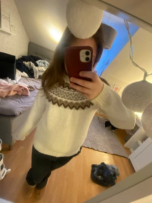 Vit stickad tröja med mönster - Säljer en mysig vit stickad tröja med rund hals och klassiskt nordiskt mönster i brunt och beige runt oket. Tröjan har långa ärmar och ribbstickade muddar. Perfekt för kalla dagar och ger en riktigt cozy vibe.
