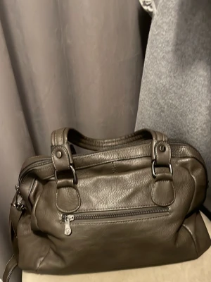 Mörkbrun väska från Puccini - Snygg mörkbrun handväska i skinnimitation med dubbla handtag och silverfärgade metalldetaljer från Puccini. Väskan har dragkedja framtill och på baksidan, samt flera fack för smart förvaring. Perfekt för dig som vill ha en stilren och rymlig väska. Hör av dig vid intresse!☺️