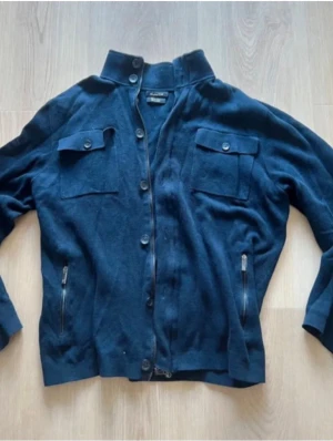 Massimo dutti cardigan - Mörkblå cardigan jacka från Filippa K med ståkrage, knäppning framtill och två bröstfickor med lock och knappar. Jackan har även två sidofickor med dragkedja och är långärmad. Perfekt för lager på lager och stilren look.