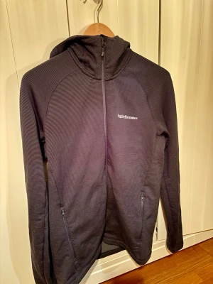 Mörkblå  zip-hoodie från Peak Performance - Snygg marinblå  zip-hoodie från Peak Performance. Tröjan har huva, hel dragkedja och två fickor med dragkedja framtill. Perfekt för lager-på-lager och outdoor-aktiviteter.