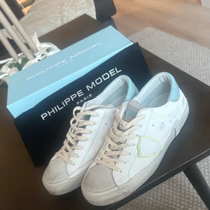 Philippe Model vita sneakers med blå detalj - Säljer ett par snygga Philippe Model sneakers i vitt skinn med ljusblå detalj vid hälen. Använda ett fåtal gånger endast, max 5 gånger