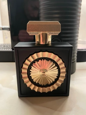 Lattafa Nebras Pride Parfym 100ml - Lattafa Nebras Pride parfym i en elegant svart flaska med gulddetaljer och geometriskt lock. Flaskan har en unik dekorativ front med solinspirerat mönster i guld och mattsvart finish. Texten på flaskan är i guld och arabiska tecken ger en exklusiv känsla. Oanvänd! Dock ingen förpackning kvar.