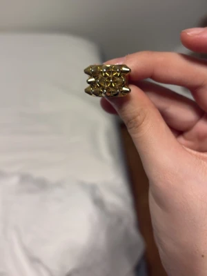 Bred guldfärgad ring med nitar - Cool bred ring i guldfärgad metall med ett mönster av små nitar och pyramidformade detaljer. Ringen har en chunky design som verkligen sticker ut och ger en edgy vibe till din stil. Perfekt för dig som gillar statement-smycken och vill ha något unikt på fingret.