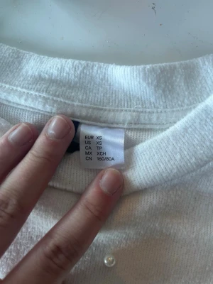 Vit t-shirt med pärlor från H&M - Säljer en vit t-shirt från H&M i storlek XS. T-shirten har korta ärmar och är dekorerad med små pärlor över hela framsidan för en extra snygg touch. Tillverkad i mjuk bomull som känns skön mot huden. Perfekt för dig som gillar detaljer!