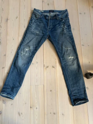 Dondup jeans - Säljer ett par blå jeans med slitningar och lätt tvättad look. Jeansen har raka ben, klassisk femficksmodell och detaljer som ger en avslappnad streetkänsla. Perfekta för dig som gillar en casual och trendig stil.