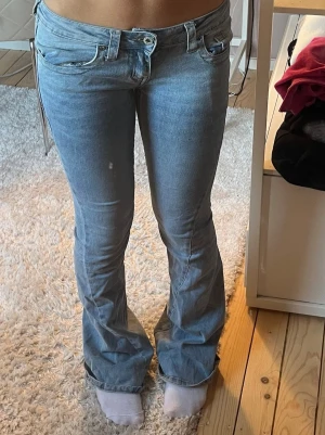 Ljusblå bootcut jeans - Säljer ett par ljusblå bootcut jeans med låg midja och klassiska fem fickor. Jeansen har en snygg tvätt och sitter tight upptill med utsvängda ben. Perfekta för en avslappnad och trendig look. Slitna nere vid fötterna men inget som syns vid andvändnig.