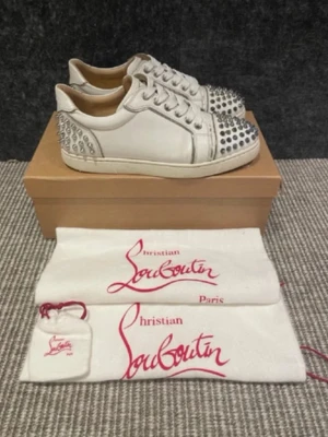 Vita Christian Louboutin sneakers med nitar - Säljer ett par vita sneakers från Christian Louboutin med silverfärgade nitar på tå och häl. Köpta på plick men var fel storlek. Kan gå ner i pris vid snabbaffär! 