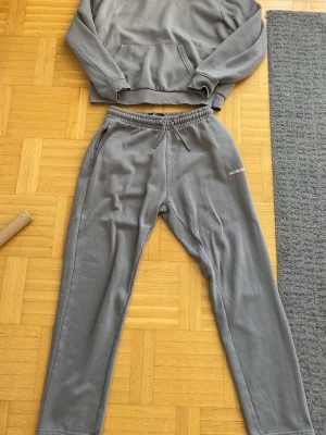 Grå mjukisbyxor från McKenzie storlek M - Snygga grå mjukisbyxor från McKenzie med broderad logga på benet. Byxorna har elastisk midja med dragsko och är tillverkade i mjukt bomullsmaterial. Perfekta för en avslappnad och chill stil.