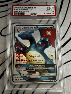 Charizard GX Pokémonkort PSA 10 - Säljer ett Charizard GX-kort från Hidden Fates, graderat PSA 10 GEM MT. Kortet är holografiskt med färger i svart, rött och blått, och ligger i en skyddande plastkapsel. Perfekt för samlare som gillar Pokémon och unika kort. OBS KORTET ÄR FEJK