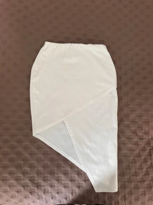 Vit asymmetrisk kjol - Snygg vit kjol med asymmetrisk skärning och enkel design. Kjolen har en unik form med snedskuren nederkant som ger en modern look. Fläckar som jag inte försökt få bort (syns på bilderna)