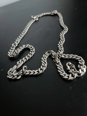 Silverfärgat kedjehalsband - Säljer ett stilrent halsband i silverfärgad metall med platta, breda länkar i klassisk kedjedesign. Halsbandet har ett robust lås och passar perfekt för dig som gillar en clean och modern look. Inget märke synligt på halsbandet.