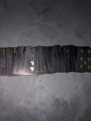 Svart kortlek med gulddetaljer - Säljer en unik kortlek med svarta spelkort och guldfärgade symboler. Baksidan har ett glansigt, ormliknande mönster som ger en lyxig känsla. Perfekt för pokerkvällar eller samlare som vill ha något annorlunda i sin samling. Skriv privat för mer bilder